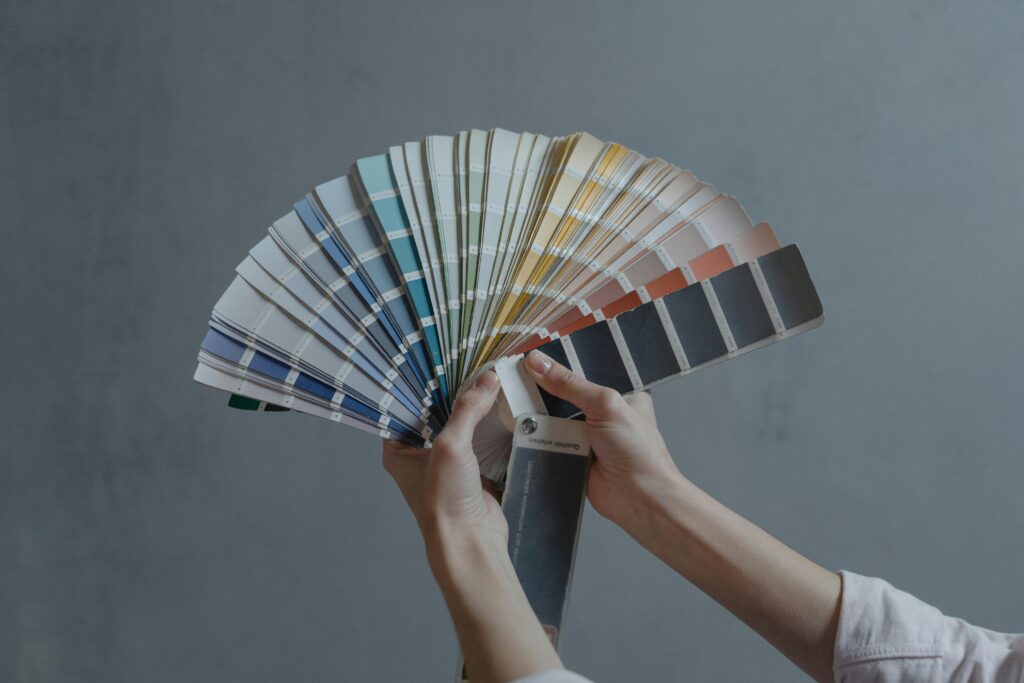 Two hands holding a fan of colour swatches spread out in a semicircle, showing a wide range of colours.